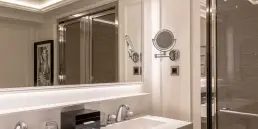 Fotografía de interiores profesional de un baño de lujo en el Hotel Sofitel Barcelona, mostrando el amplio espejo iluminado y el detalle de la ducha con mampara de cristal.