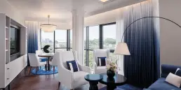Fotografía de interiores profesional de una suite de lujo en el Hotel Sofitel Barcelona, capturando el salón con sofás azules, butacas blancas y vistas panorámicas.