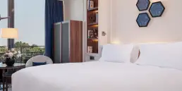 Fotografía de interiores profesional de una suite de lujo en el Hotel Sofitel Barcelona, mostrando el área de la cama con ropa de cama blanca, estanterías integradas e iluminación ambiental.