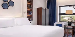 Fotografía de interiores profesional de una suite en el Hotel Sofitel Barcelona, mostrando la cama, zona de lectura con mesa y butacas, y ventanal con vistas.