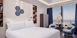 Fotografía de interiores profesional de una suite en el Hotel Sofitel Barcelona, mostrando la cama, el diseño de la habitación y un gran ventanal con vistas al mar Mediterráneo.