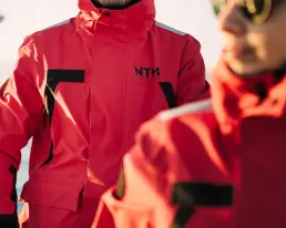 Dos personas con chaquetas técnicas rojas de NTN Ocean Wear en un velero, representando el contenido digital ecommerce producido por LUP Studio.